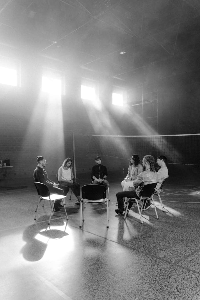 A diverse group of people sit in a circle, engaged in a discussion in a sunlit room.